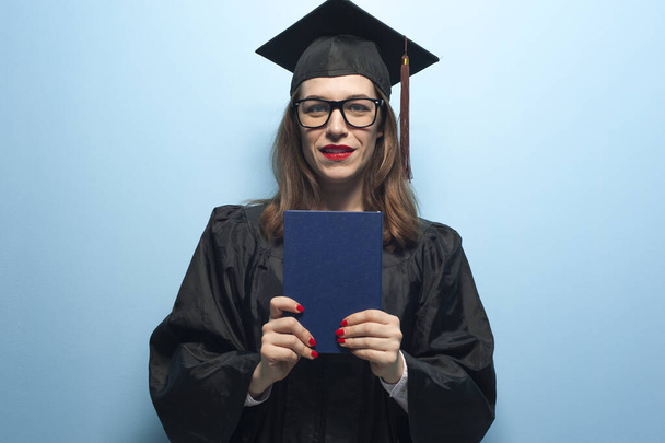 Charming female student wearing black mantle and standing with diploma in hands - Photo, Image