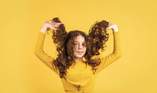 Little child curly hair. Fashion and beauty. Professional cosmetics. Freedom self expression. Girl hairdresser salon. Hairstyle party. Hairdresser supplies. Brushing long hair. Enjoying shiny curls - Фото, зображення
