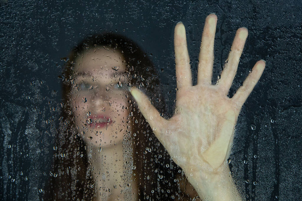 Imagen de una joven tocando el vidrio con gotas de agua - Foto, imagen