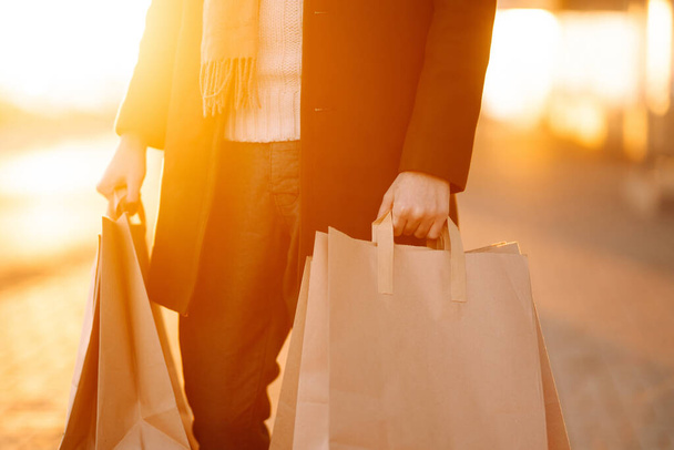 Hand of young man with paper bags with purchases at sunset. Young man after autumn shopping. Consumerism, shopping, black friday, sales, lifestyle concept. - Φωτογραφία, εικόνα