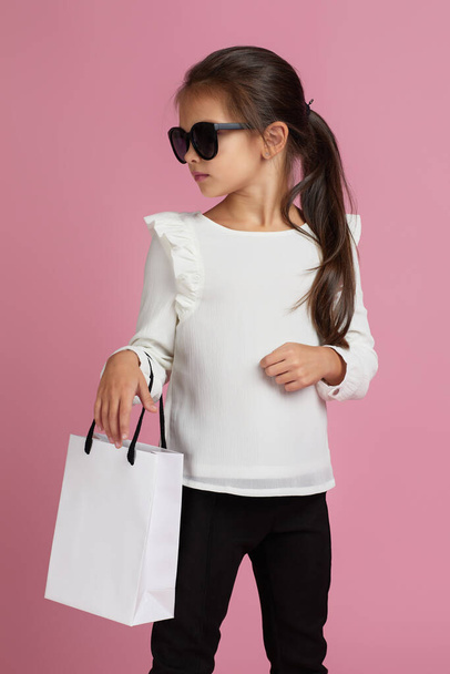 child girl in sunglasses is holding shopping bags - 写真・画像