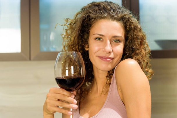 Attractive friendly young woman with a lovely warm smile toasting the camera with a large elegant glass of red wine to celebrate in a close up portrait - Photo, Image