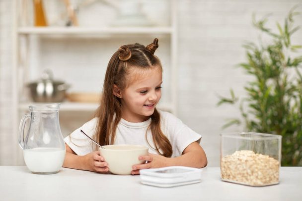 little girl eating breakfast: cereal with the milk in the kitchen. - Φωτογραφία, εικόνα