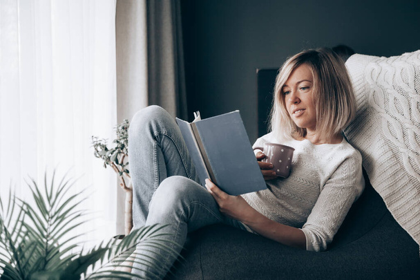 Relaxante mulher lendo um livro e bebendo chá em casa - Foto, Imagem