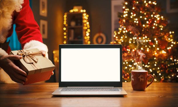 Santa Claus bringing a gift at home on Christmas eve and blank laptop - Foto, afbeelding