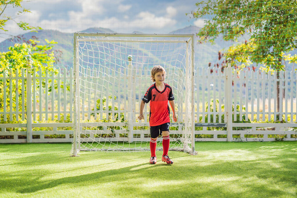 Little cute kid boy in red football uniform playing soccer, football on field, outdoors. Active child making sports with kids or father, Smiling happy boy having fun in summer - Fotografie, Obrázek
