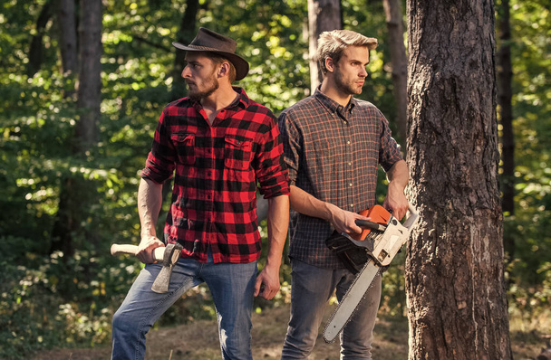 hiking in deep wood. forest care at vacation. summer or spring activity. man farmers relax in forest. rangers use lumberjack equipment. Lumberjack with chainsaw and ax. Harvest firewood - Фото, изображение
