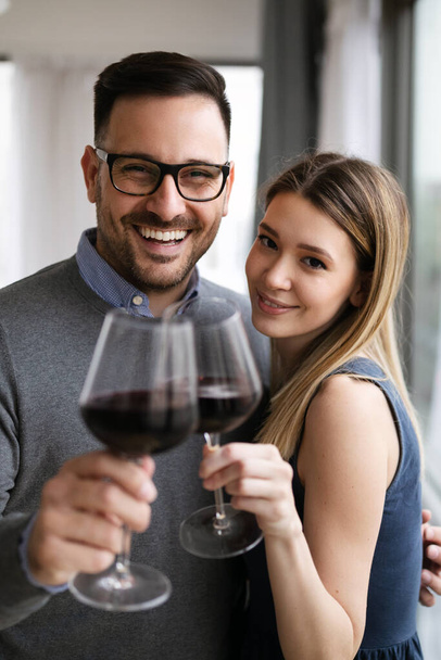 Happy beautiful couple in love hugging and drinking red wine at home - Foto, afbeelding