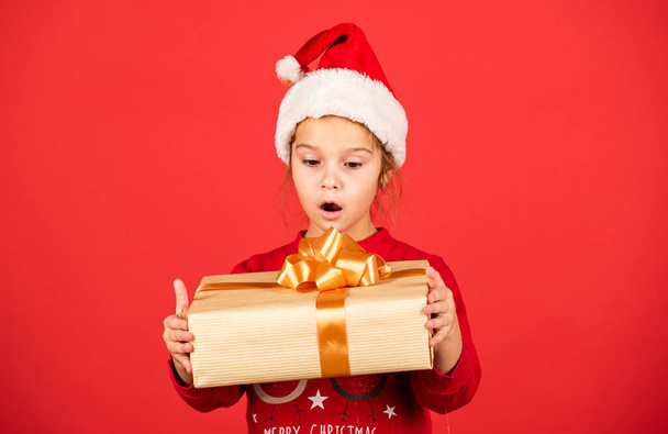 Unbelievable. Amazing surprise. Merry Christmas and happy holidays. Winter holidays. Xmas gift shopping. Gift package. Small adorable girl Santa hat hold gift box. Kid hold present box red background - Foto, afbeelding
