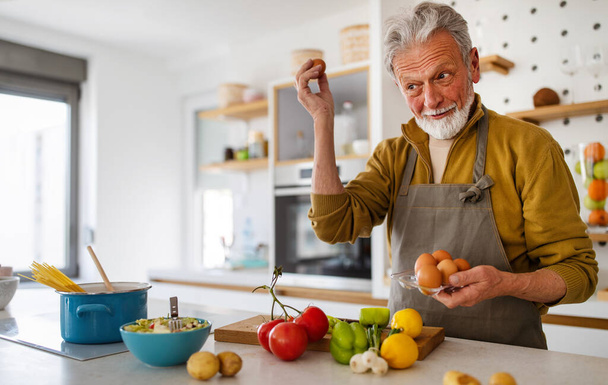 Happy retired mature man cooking in kitchen. Retirement, hobby people concept - Foto, immagini