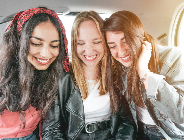 Junge freundliche Mädchen haben Spaß mit Smartphone im Auto - fröhliche multiethnische Gruppe genießt Freizeit im Freien mit Telefon - Urlaub mit Freundinnen - Foto, Bild