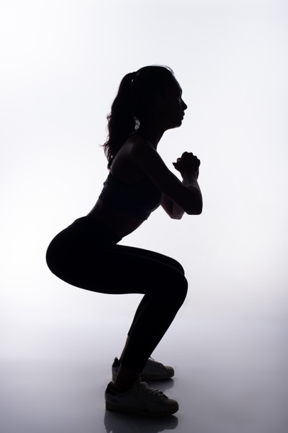 Silhouette slanke body van Young Fitness Woman beslaat haar benen voor het trainen in volledige lichaamslengte. Hoge contrast witte achtergrond kopiëren ruimte - Foto, afbeelding