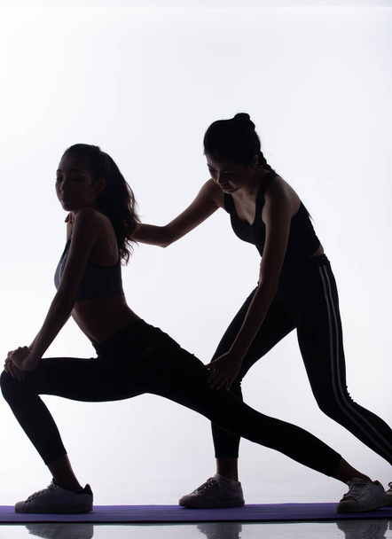 Silhouette slim body of two Young Fitness Women play Yoga, exercise Stretch arms legs and friend support as coach. High contrast white background copy space - Foto, afbeelding