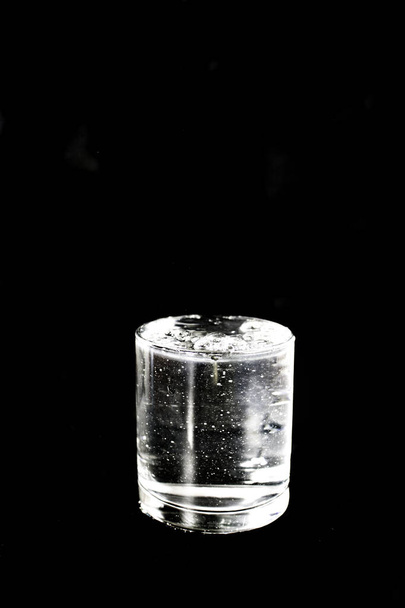 Pełna szklanka wody na czarnym tle. Zdjęcie wykonane z selektywnym ukierunkowaniem i efektem szumu - Zdjęcie, obraz