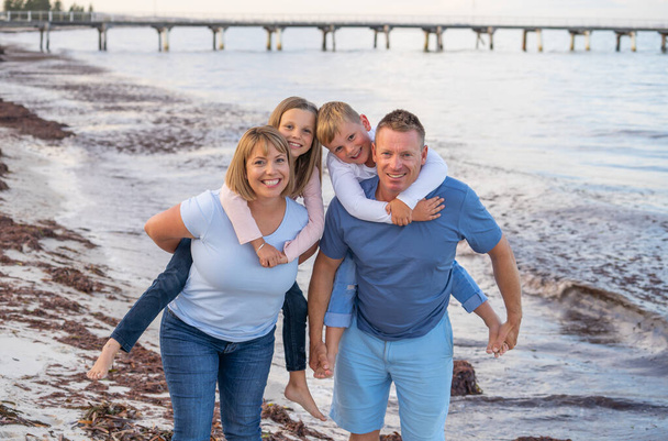 Outdoors portrait of a happy family of four members, mom, dad, and children boy and girl, embracing and having fun together at the beach. Happy moments, vacations and holiday portrait concept. - Fotoğraf, Görsel