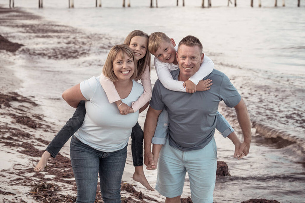 Outdoors portrait of a happy family of four members, mom, dad, and children boy and girl, embracing and having fun together at the beach. Happy moments, vacations and holiday portrait concept. - Foto, imagen