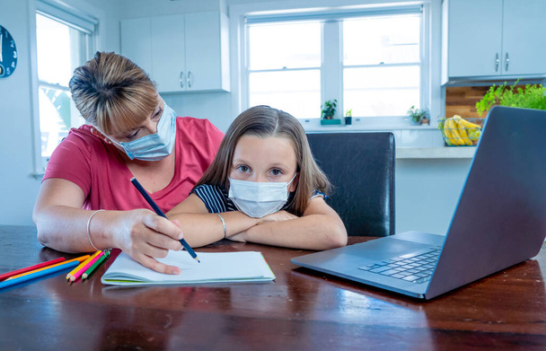 Stressed Mother helping bored daughter studying online lesson at home. Parent and child with face mask homeschooling during second lockdown, self isolation or School closures due to COVID-19 Outbreak. - Foto, Imagen