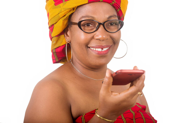 volwassen vrouw in traditionele jurk staan op witte achtergrond communiceren op mobiele telefoon en kijken naar camera glimlachen. - Foto, afbeelding