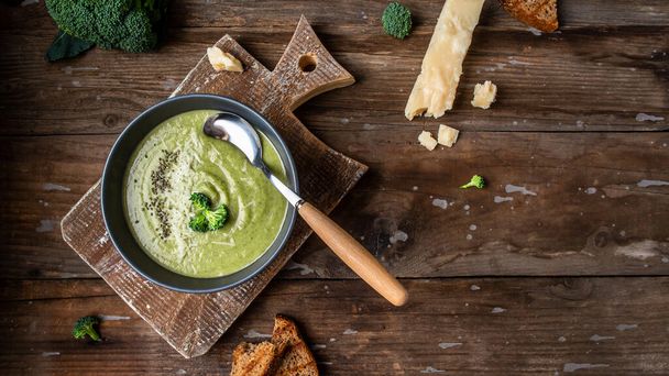 bowl of broccoli cream soup with parmesan cheese and crunchy croutons on wooden table, top view. - Foto, Imagem