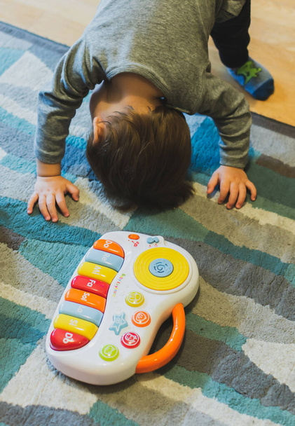 POZNAN, POLONIA - 27 ottobre 2018: Tastiera musicale giocattolo di plastica appoggiata su un tappeto accanto a un bambino in uno sfondo soft focus. - Foto, immagini