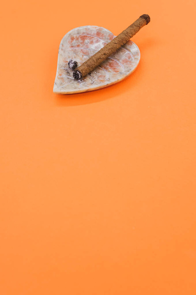 A vertical shot of a cigar on an ashtray on an orange surface - Foto, Imagen