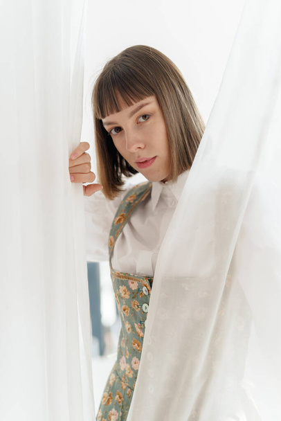 young girl in old fashione clothes posing near the window  - 写真・画像