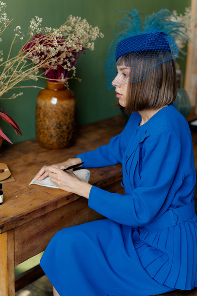 νεαρή γυναίκα με μπλε παλιομοδίτικο φόρεμα γράφει ένα σημείωμα - Φωτογραφία, εικόνα