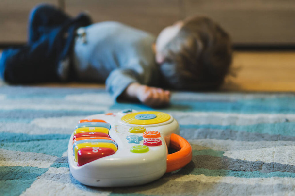 POZNAN, POLAND - Oct 27, 2018: Plastic toy music keyboard laying on a carpet next to a child in soft focus background. - Foto, Imagen