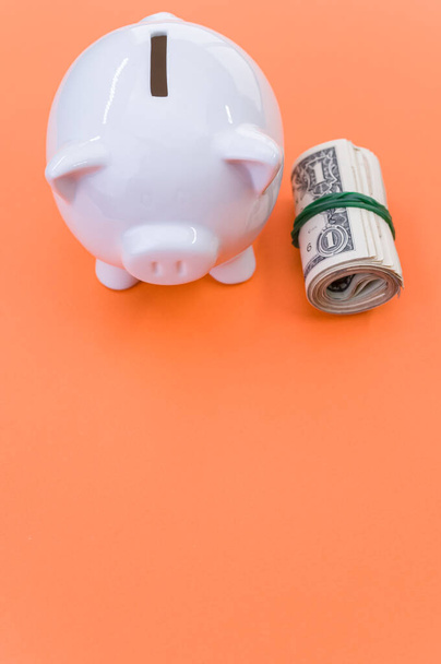 A vertical shot of dollar bills and a piggy bank on an orange surface - Zdjęcie, obraz