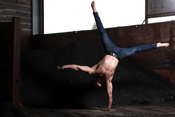 Young Man Keeping Balance on Hand in Warehouse - Muscular Athletic Bodybuilder Fitness Model Doing Handstand Push-up - Foto, afbeelding