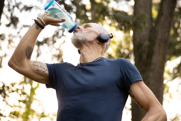 Athletic male quenching thirst during workout outdoors - Фото, зображення