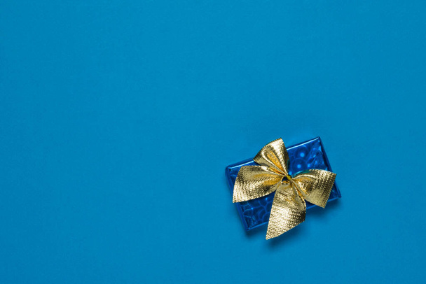Blaue Schachtel mit einem Geschenk in goldenem Band auf blauem Hintergrund. - Foto, Bild