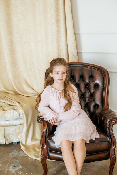 Lovely and elegant girl with long fair hair, in beautiful fashionable dresswith hairstyles in a classic light interior . Beauty and fashion. Children fashion - Zdjęcie, obraz