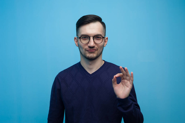 Portrait of an emotional young man in glasses showing Okey gesture - Foto, Imagen