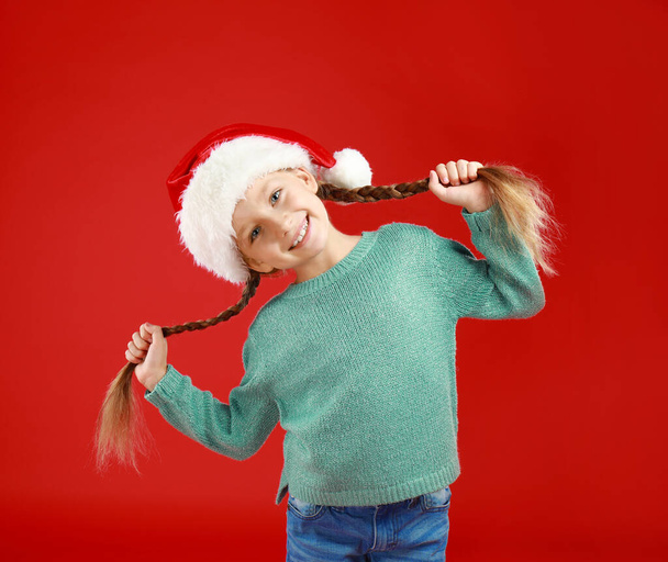 Happy little child in Santa hat on red background. Christmas celebration - Fotó, kép