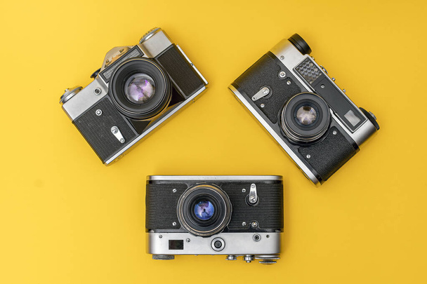 Tres viejas cámaras de cine yacen sobre un fondo amarillo en forma de triángulo - Foto, Imagen