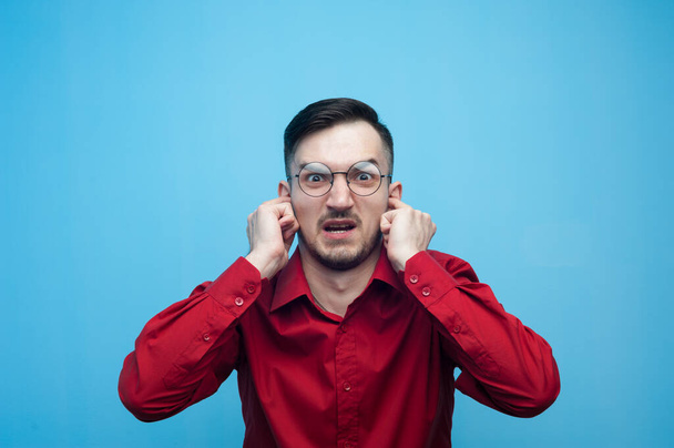 Man wearing red shirt and glasses covering his ears with hands. - Φωτογραφία, εικόνα