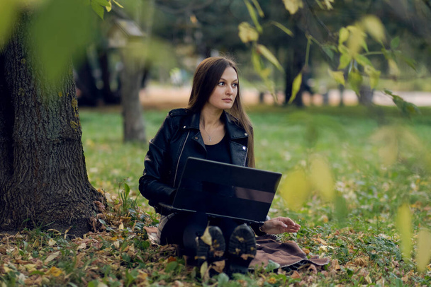 Die junge Frau arbeitet für einen Laptop im Park. der Student bereitet sich auf Prüfungen vor - Foto, Bild
