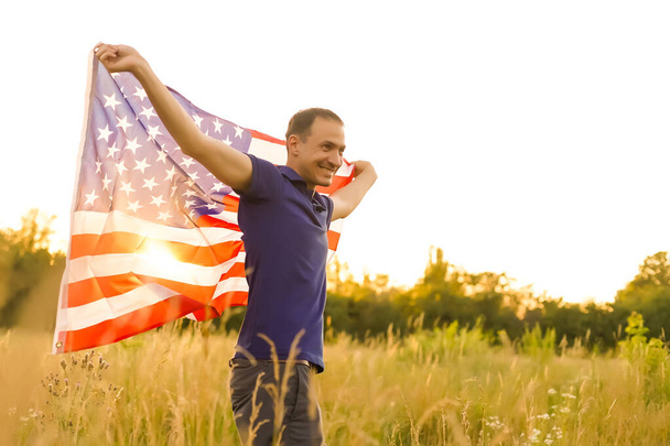 4 Ιουλίου. Πατριώτης με την εθνική αμερικανική σημαία στο πεδίο. Νεαρός άνδρας με υπερηφάνεια κυματίζει αμερικανική σημαία. Ημέρα ανεξαρτησίας. - Φωτογραφία, εικόνα