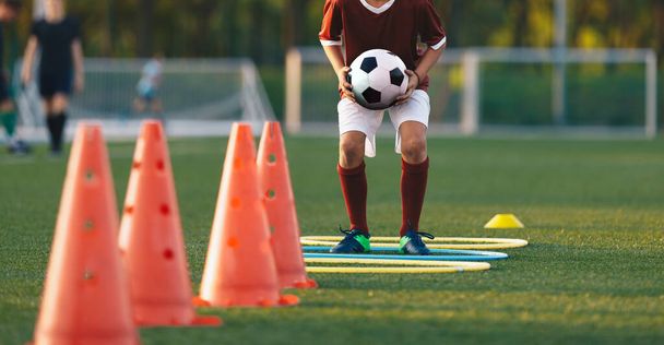 Close up boy running on football training pitch with ball in his hands. Player jumping over obstacles. Football training obstacle course. Children level soccer drill - Photo, Image