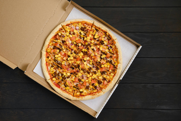 Top view of pizza with beef minced meat, tomato, onion and cheddar in cardboard package - Fotó, kép