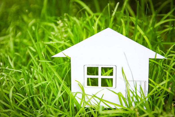 The concept or conceptual house white paper in his hand in a green summer grass on a background, a symbol for the construction, environment, credit, property or home - Φωτογραφία, εικόνα