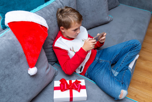 Top view Ελκυστικό παιδί αγόρι χρησιμοποιώντας το smartphone για τις διακοπές των Χριστουγέννων λευκό δώρο για τη φωτογραφία Χριστούγεννα στο σπίτι - Φωτογραφία, εικόνα