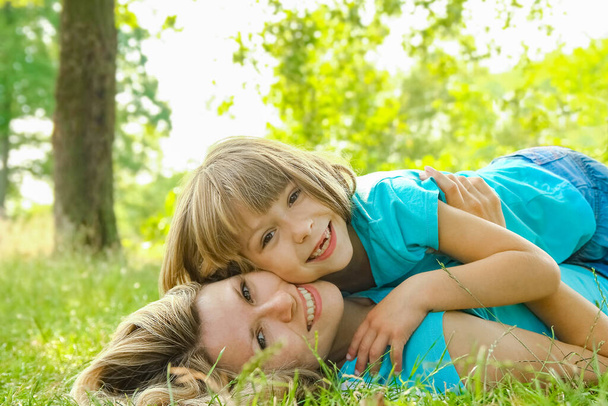 child with mother play outdoors in a park on the mother in the grass - Foto, imagen