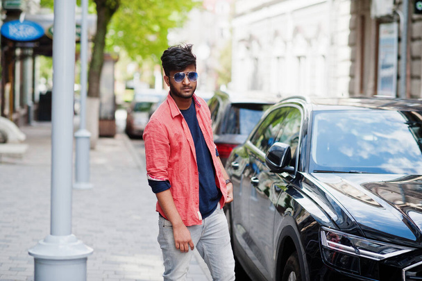 Portrét mladého stylového indického muže model pózovat na ulici v slunečních brýlích proti autu. - Fotografie, Obrázek