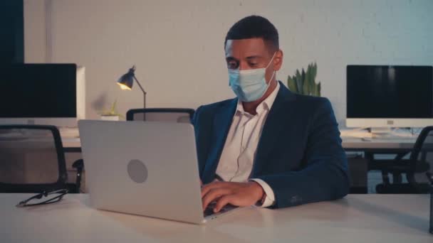 afro-amerikai üzletember orvosi maszkban gépelés laptopon az irodában  - Felvétel, videó