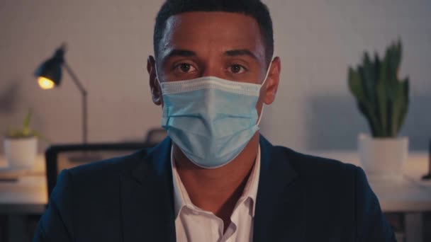 african american businessman in medical mask sitting in office at night - Imágenes, Vídeo