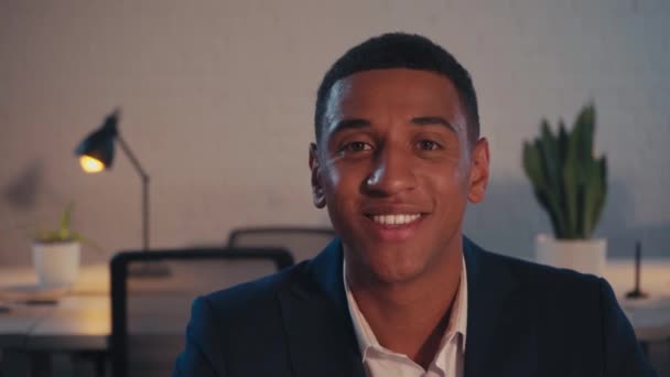 Afrykański amerykański biznesmen uśmiecha się do kamery w nocy w biurze - Materiał filmowy, wideo