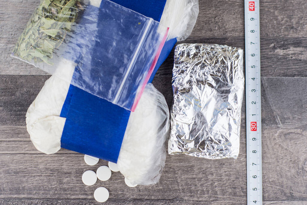 suspeita de tráfico de drogas, pílulas desconhecidas, pó branco em um pacote transparente e a folha metálica, e como uma mistura de "especiarias", estão sobre a mesa, uma régua para medir à direita - Foto, Imagem