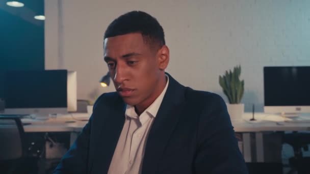 uomo d'affari afro-americano esausto toccare gli occhi vicino al computer portatile di notte - Filmati, video